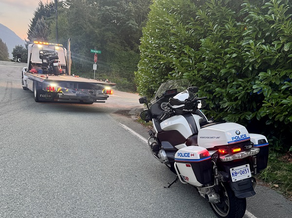 A BC Highway Patrol motorcycle is parked behind a tow truck carrying an impounded Harley Davidson in Lions Bay