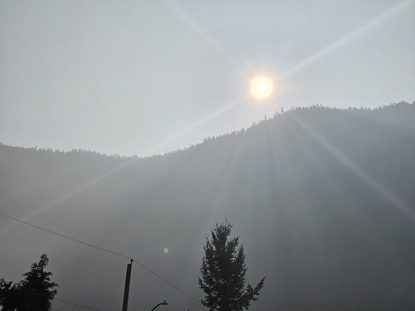 Sun shining through thick wildfire smoke over a forested mountain ridge in Squamish.